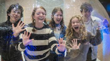 Group of 5 students inside of an inflatable Snow Globe, with their hands and faces pressed against the sides laughing and cheering in excitement during WinterFest