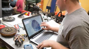 A student uses a computer at a work bench to review engine components as a part of the Alternative Energy Racing Organization club