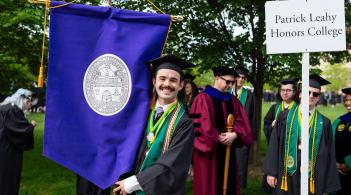 Photo of student at graduation holding blue banner with another student holding honors college sign.