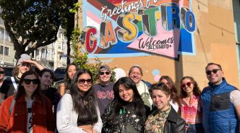 a group of UVM students and Prism staff in front of the Greetings from the Castro District sign from the Creating Change conference in 2023.