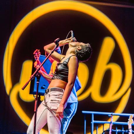 A female singer singing infront of a glowing yellow upb logo