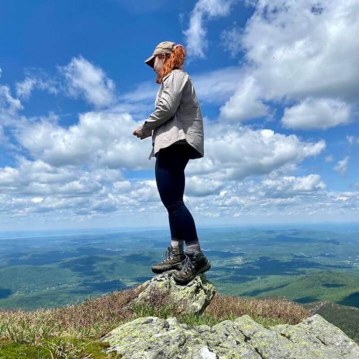 Alyssa standing on a mountain summit looking down and away