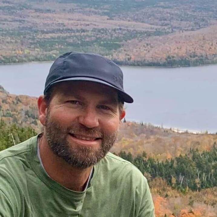 Ben in front of a forested lake in autumn