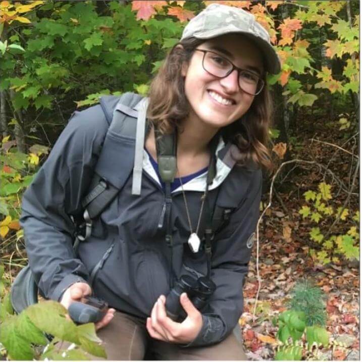Morgan kneeling on the forest floor holding a GPS