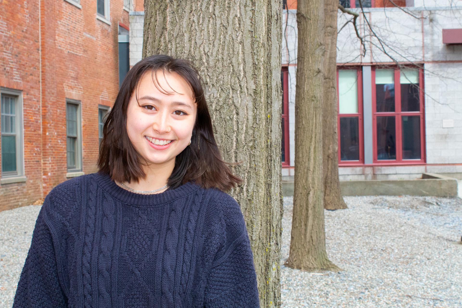 Student Aoi Tischer wearing blue sweater standing in front of tree