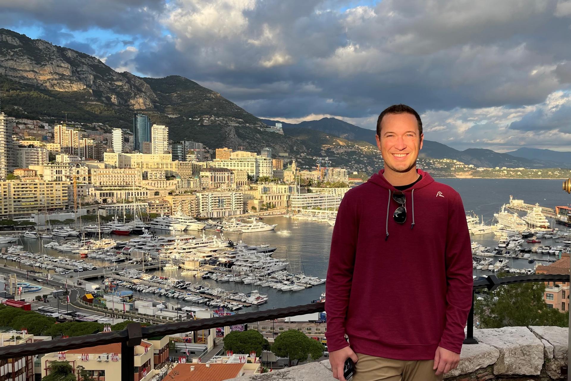 man with short dark hair and red pullover standing in front of overlook over city