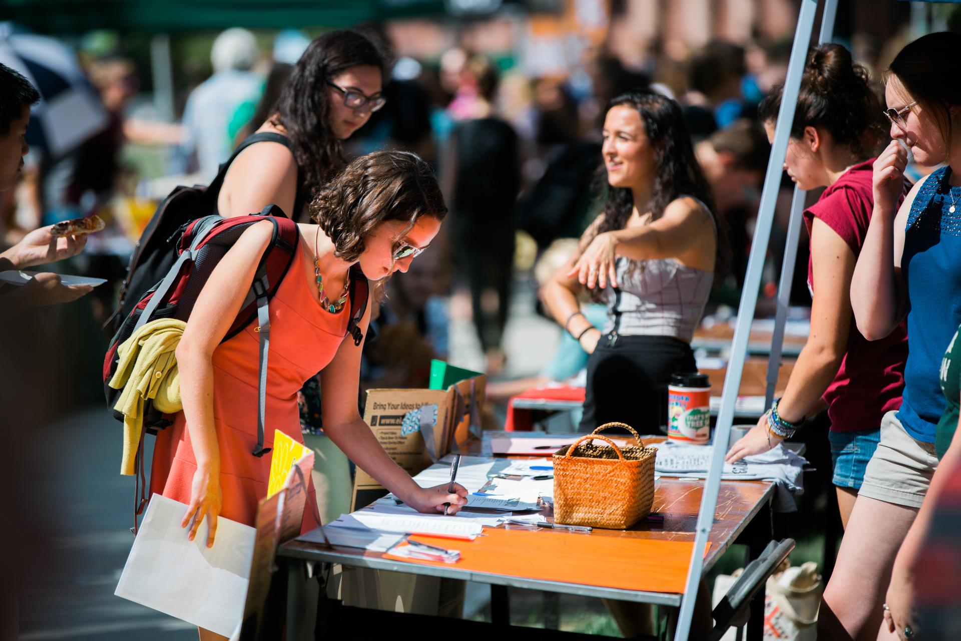 Tabling at ActivitiesFest showing a student filling out a form on a table while a table worker points at another student showing them what they're doing