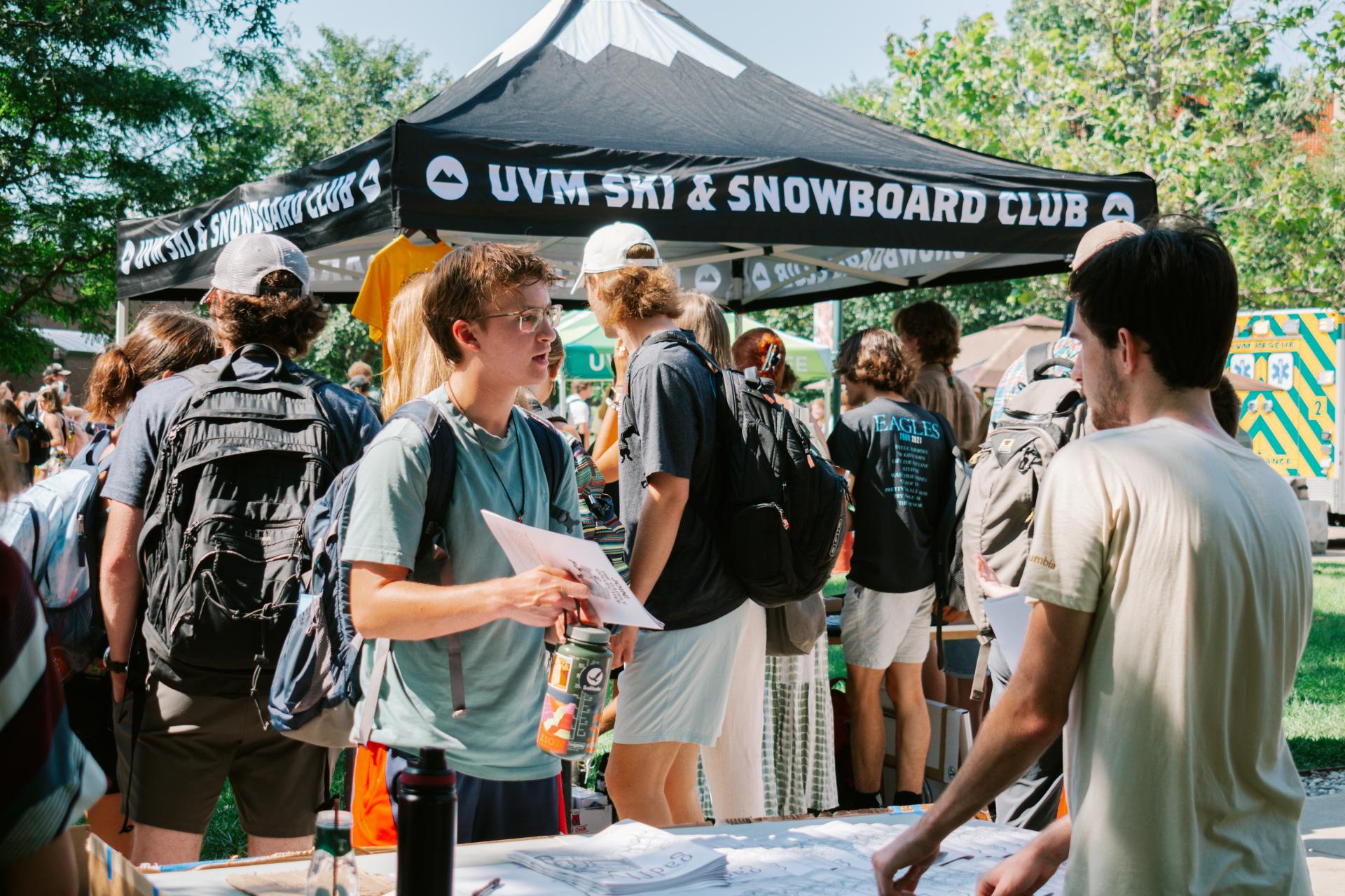 A table at the ActivitiesFest event showing a student talking to someone behind the table with many more students in the background going to the other tables around