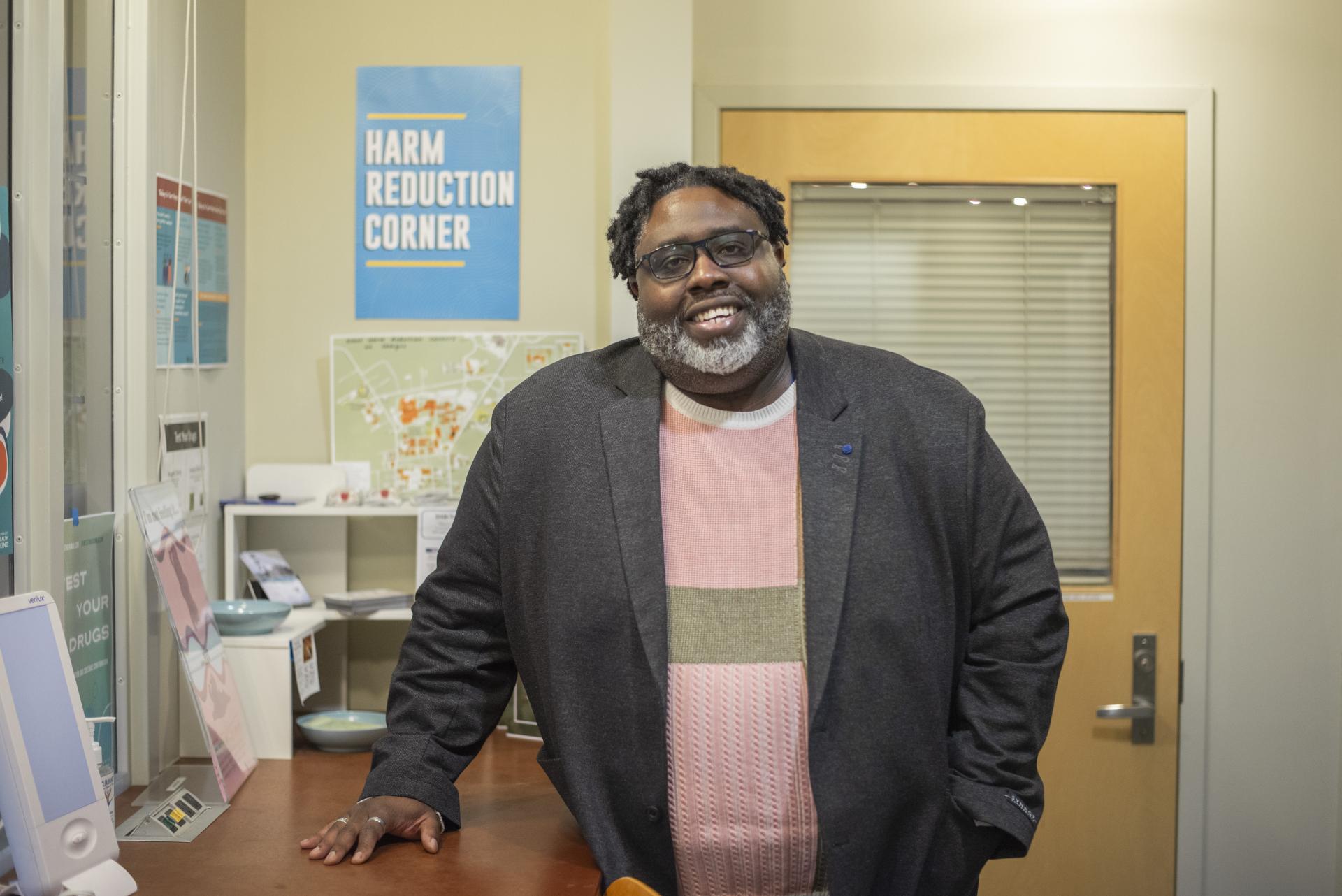 Man in a sports coat and pink sweater in front of the harm reduction corner