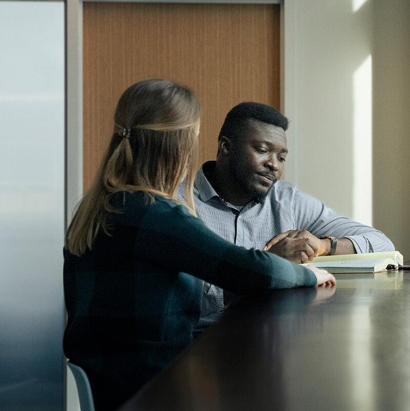 Two person sitting at a table in an office, engaged in a discussion