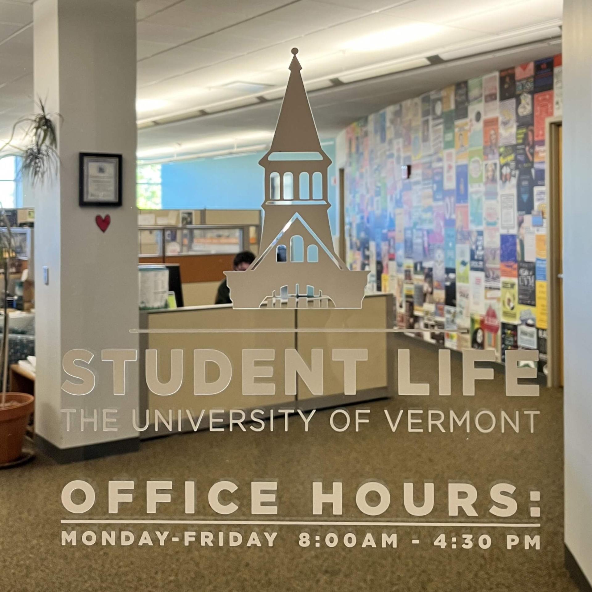 Glass door outside of the student life office with the UVM Logo and the "Student Life" logo alongside the office hours of operation