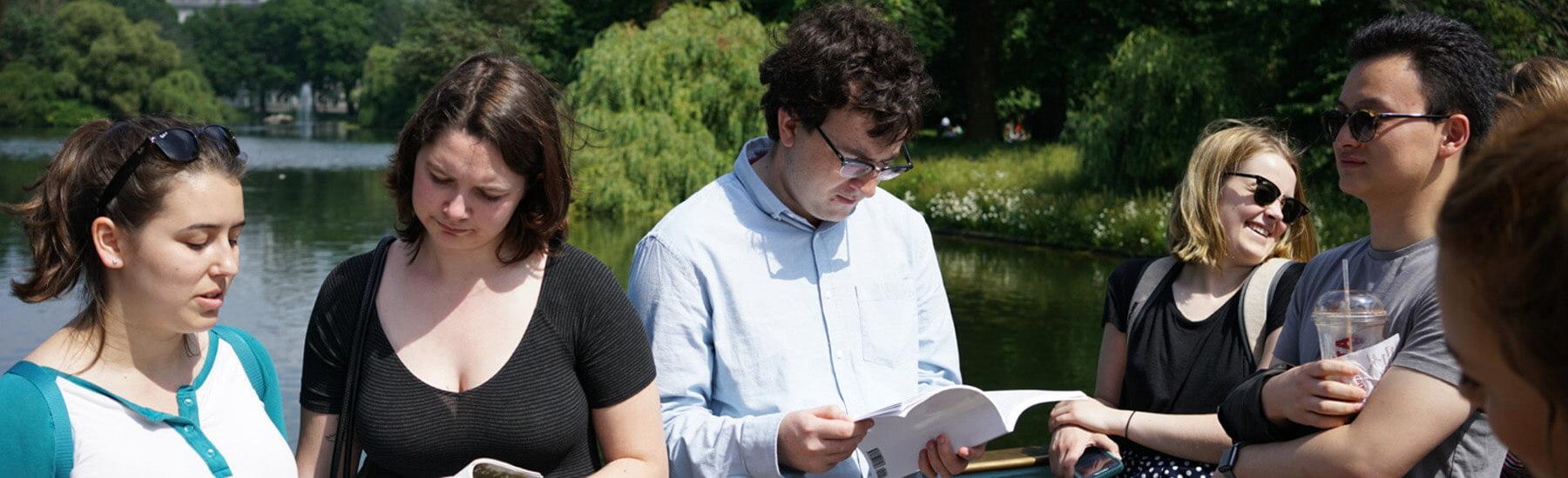 A group of people standing outside reading a book