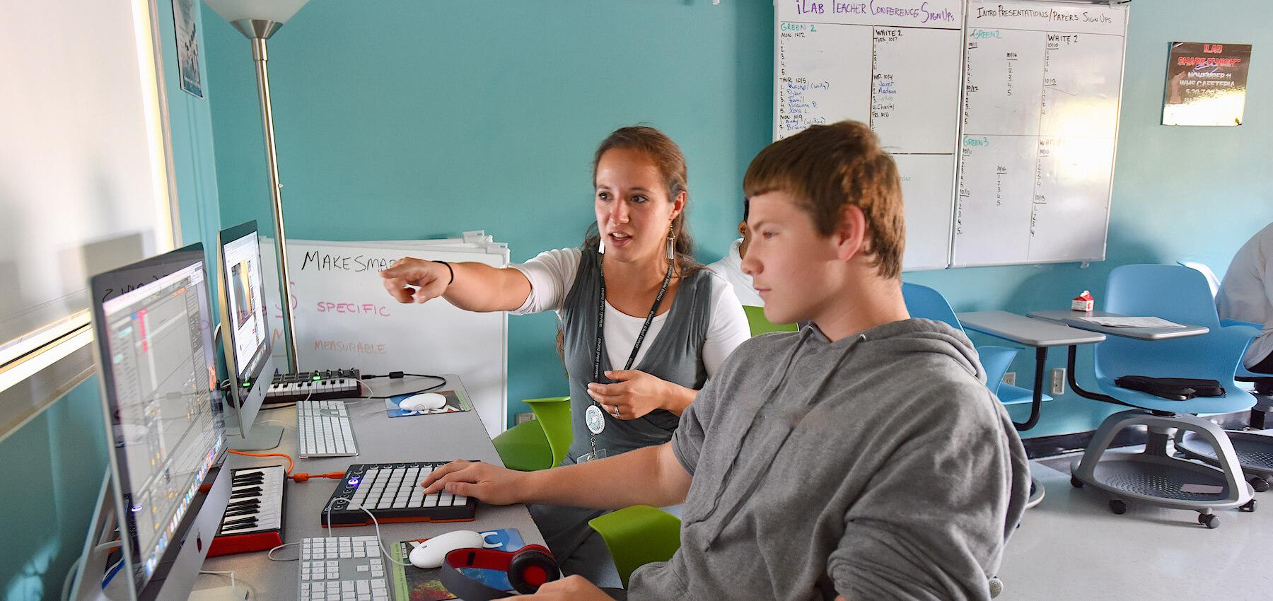 Teacher works with a high school student on computer activity in classroom.