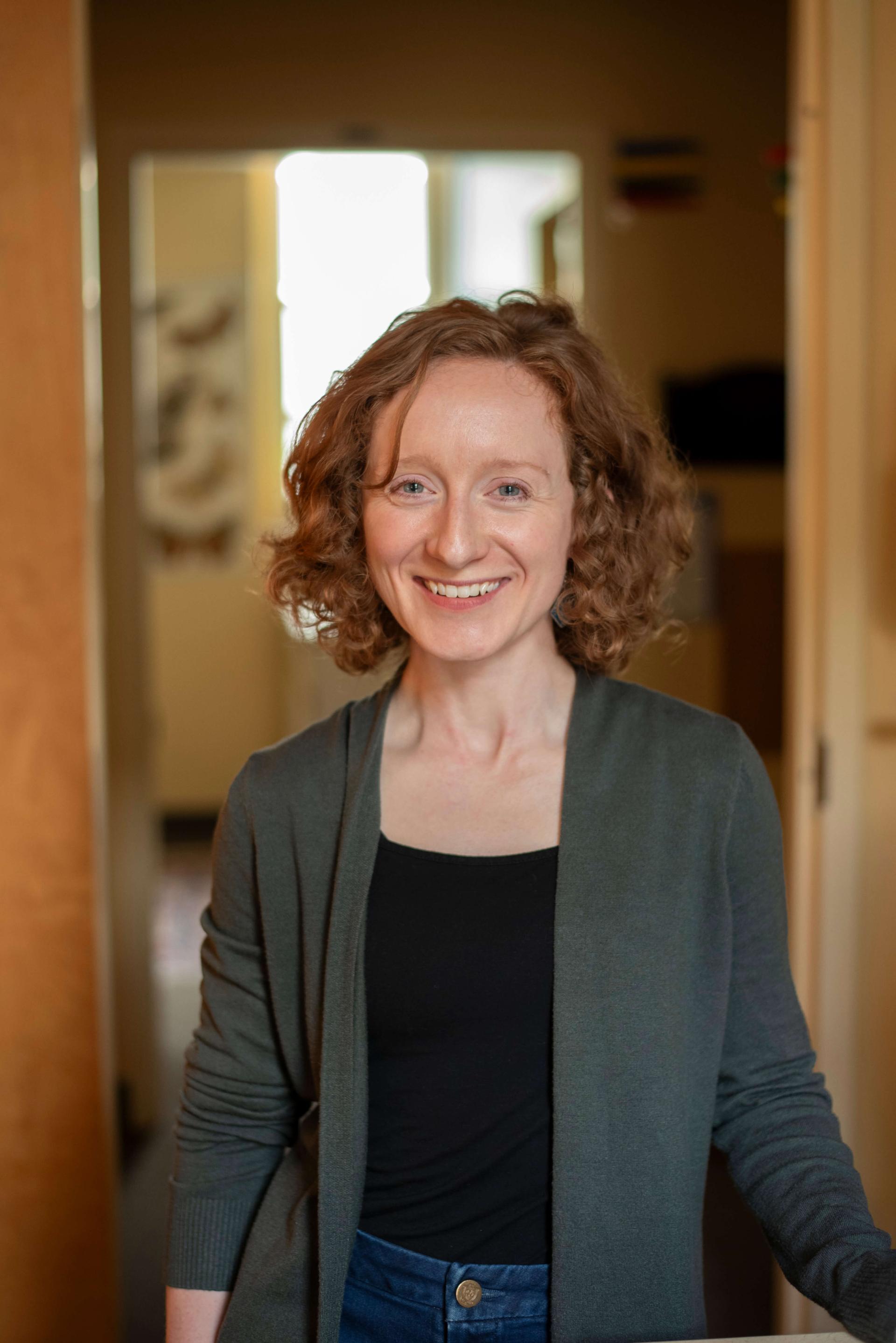 a white woman with short curly red hair stands in a doorway