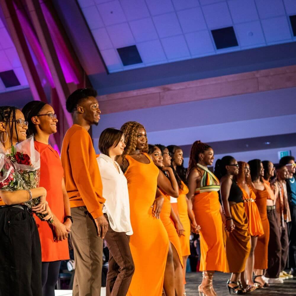 A line of well dressed students in oranges and reds from the Black Student Union thanking attendees of their Fashion Show