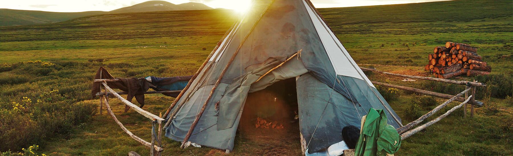 A teepee standing tall in a vast field under the clear blue sky.