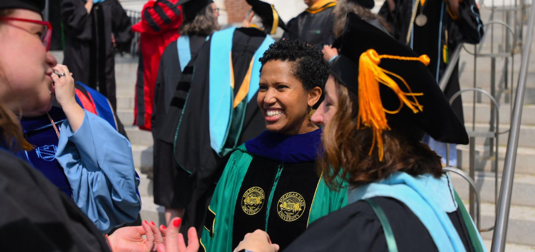Faculty smiling and talking at Commencement