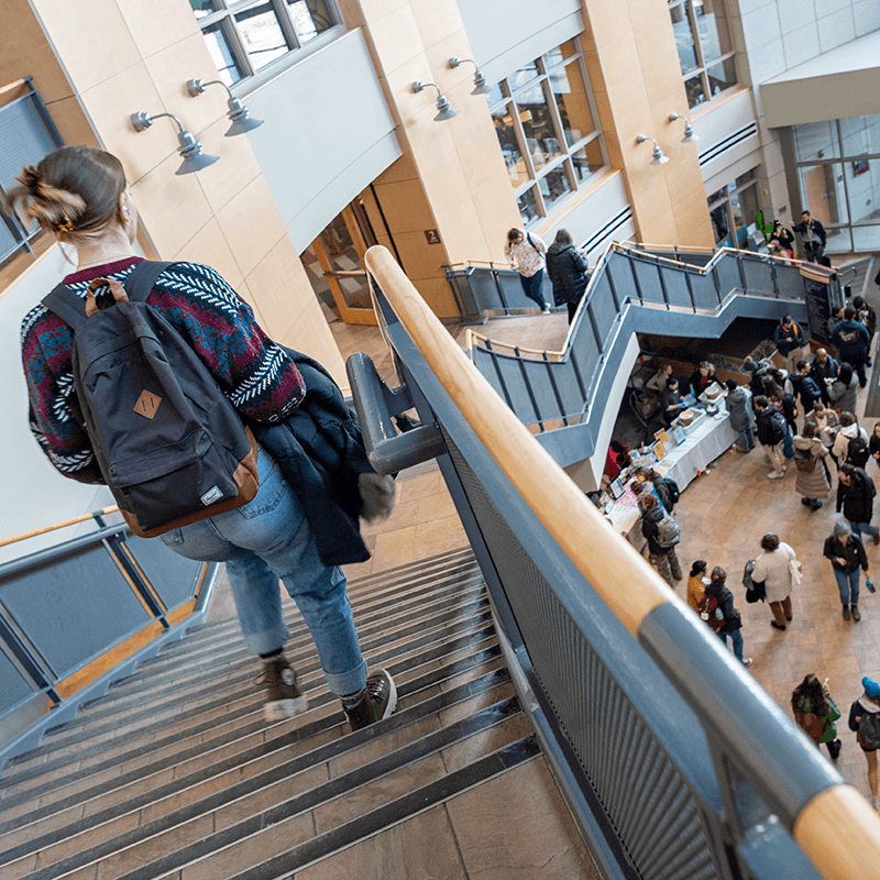 Student walking down stairs in Davis Center, crowd of people seen below in the Davis atrium. 