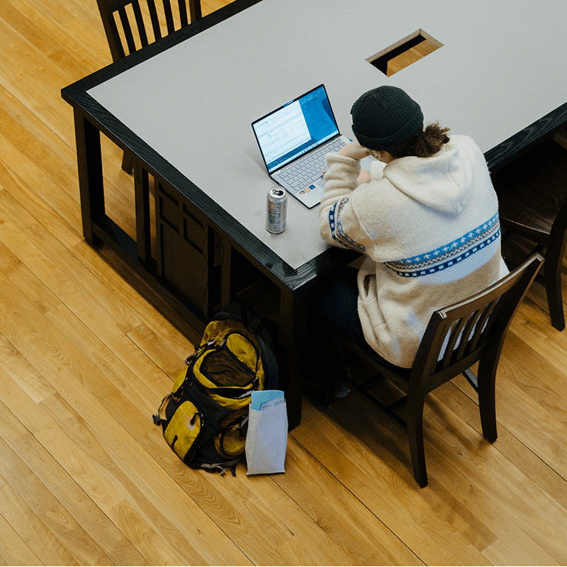 Student sitting alone at a desk in Billings with a computer and bag at their left side, image taken looking down on the student