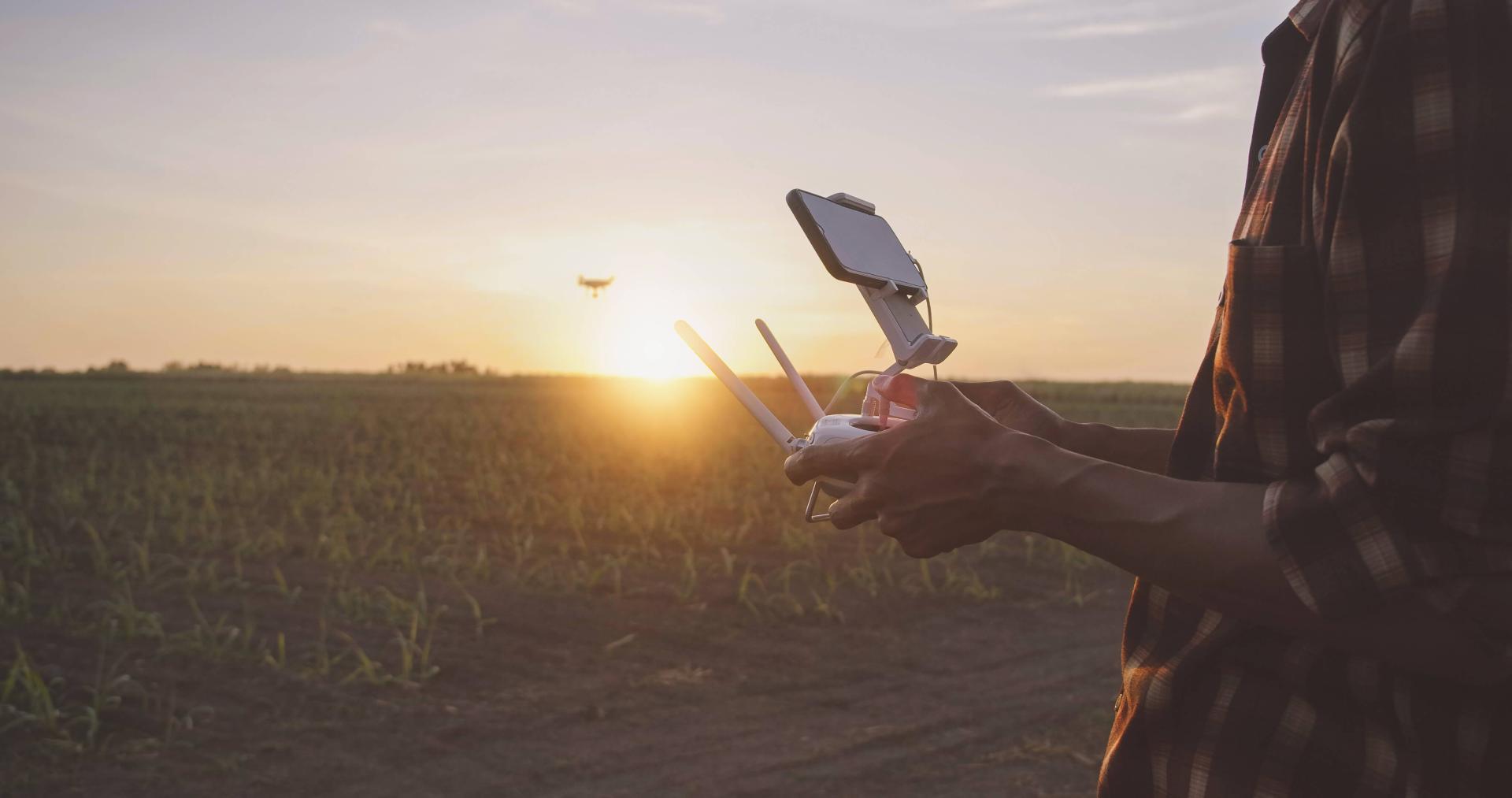 Man in a flannel flies a drone at sunset.
