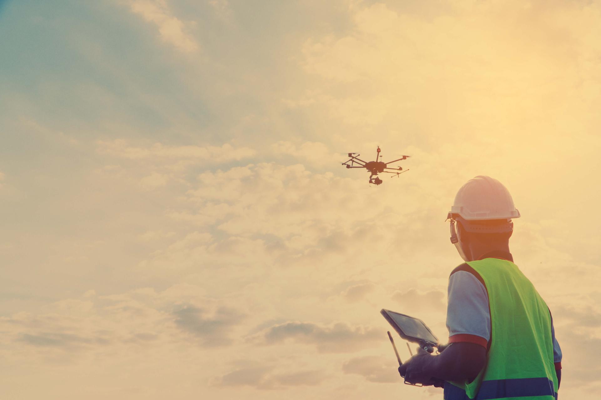Man in hardhat and safety vest flies a drone.
