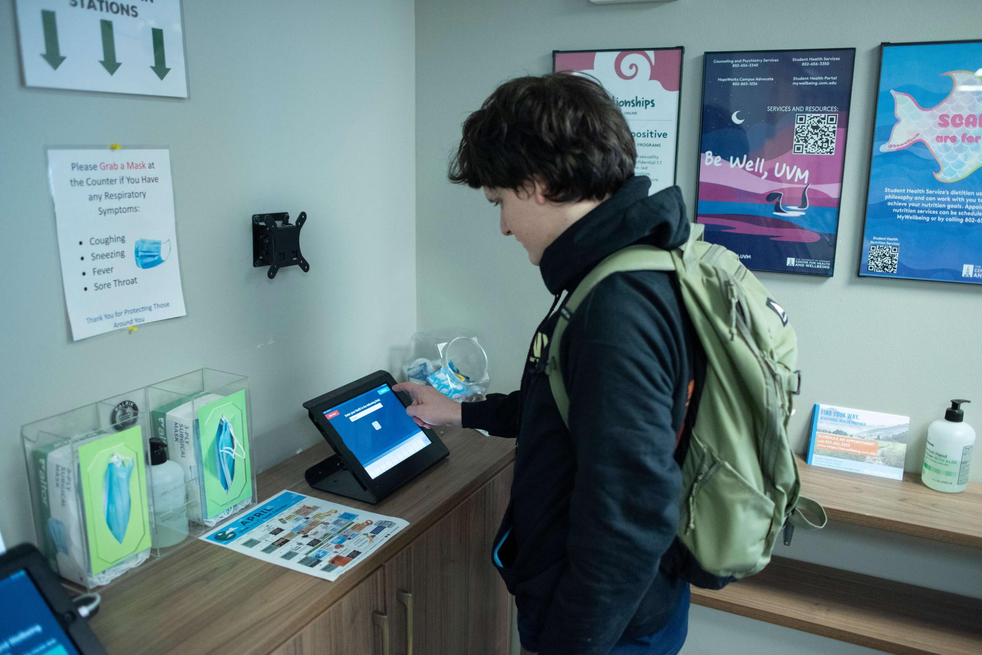 a student wearing a backpack stands at an ipad and is touching the screen