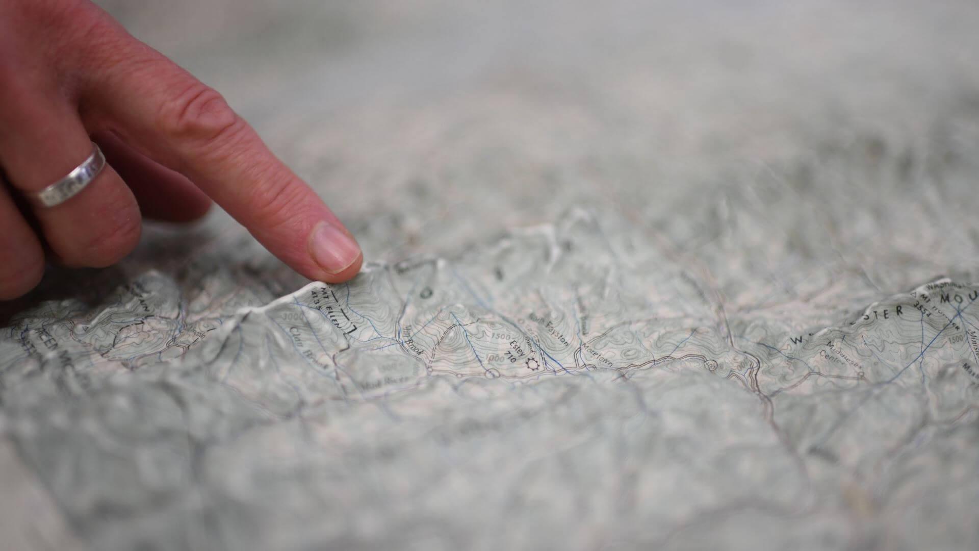 hand touching the raised ridge of a mountain on a topographic map