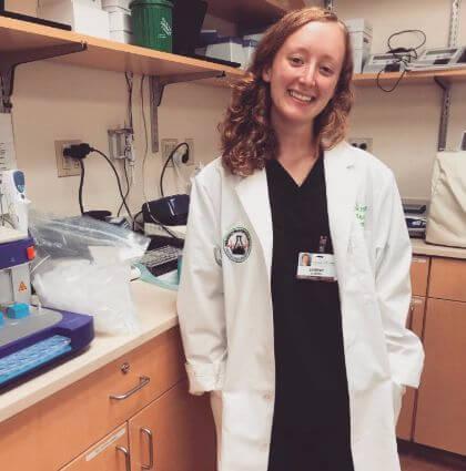 A student in a lab coat stands before a desk
