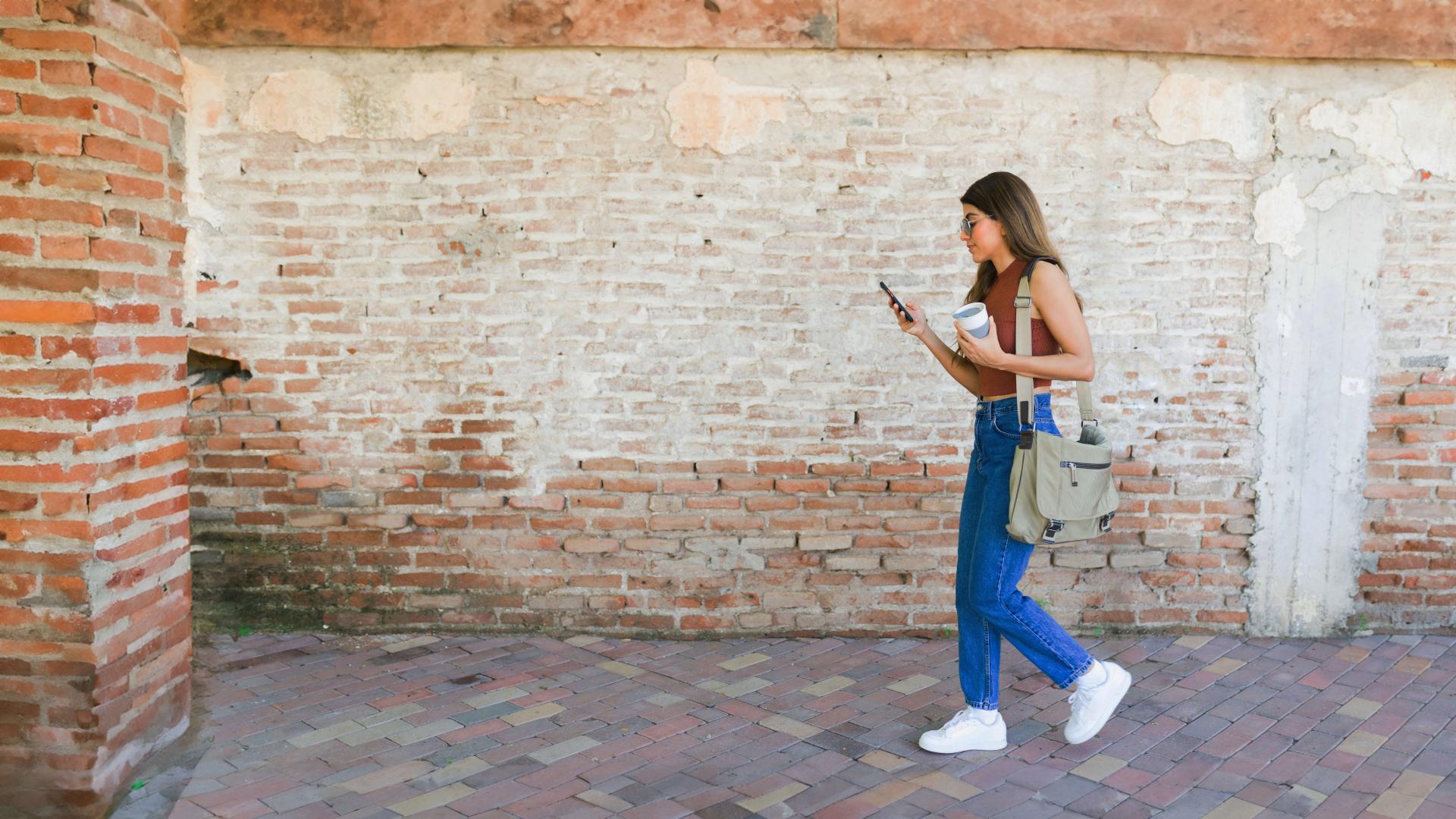 Student walking by brick wall while looking at phone.