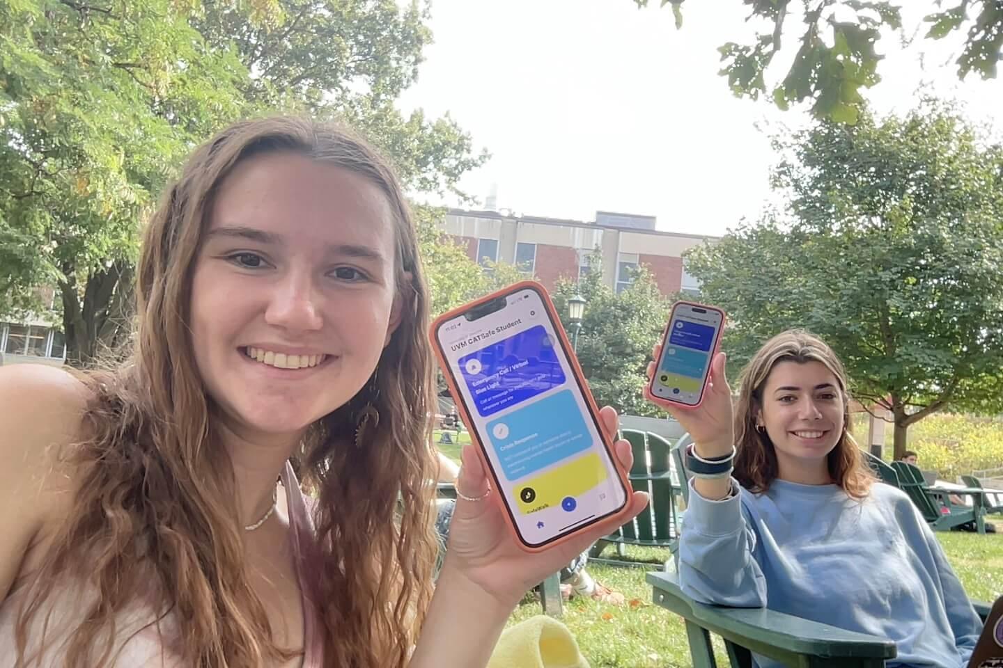 Two students sitting outside holding up iPhones with the CatSafe App visible