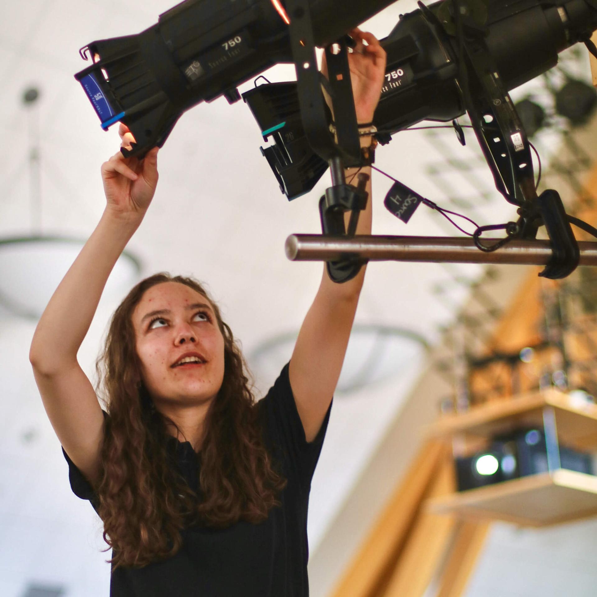 A student adjusts two spotlights in the grand maple ballroom