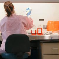 A female student in a pink lab coat conducts an experiment.