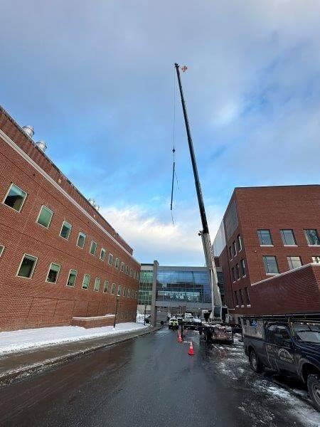 Overhead crane lifting large pipe above Stafford building