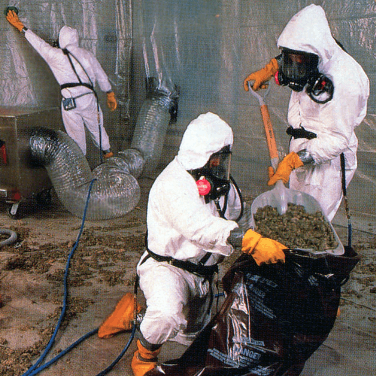 Workers in full PPE scoop asbestos into bags.