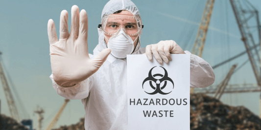 Person in full PPE holding Hazardous Waste Sign with Hand Up in a Stop Position