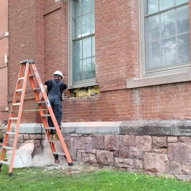 masonry worker standing on a ladder repairing brick wall