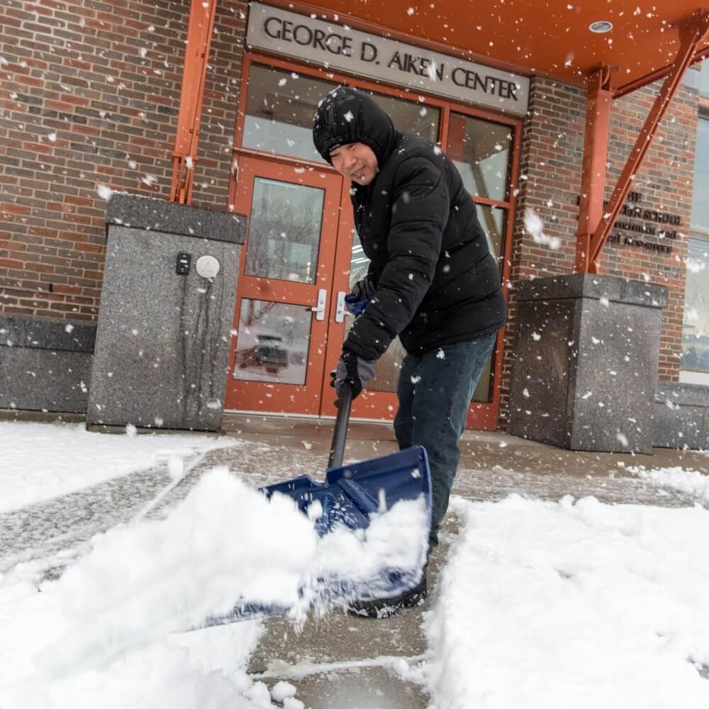 custodial worker shoveling fresh snow from sidewalk