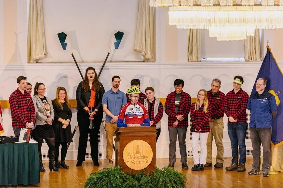 The Spatial Analysis Lab team on the stage at the memorial with Ernie Buford at the podium in a yellow bike helmet