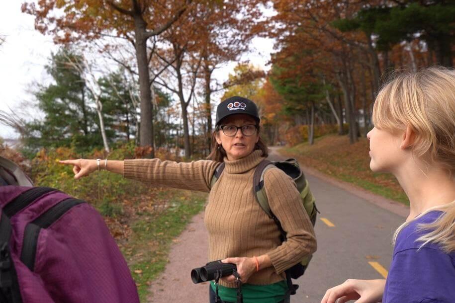 Trish O'Kane holding binoculars and pointing something out to a group of students.