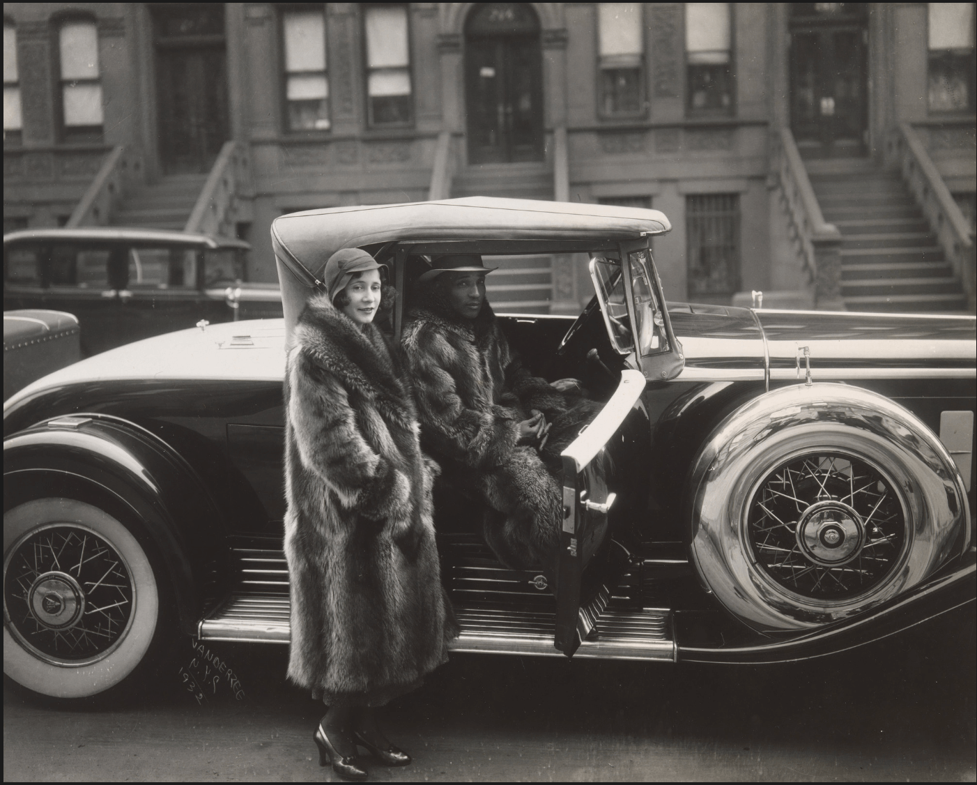 A woman in a fur coat and a man in a suit are seated together inside a luxurious car