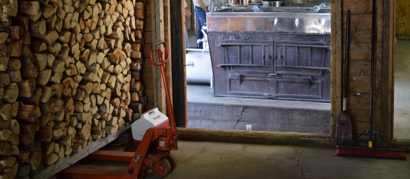 inside of a sugarhouse, with stacks of wood and an evaporator
