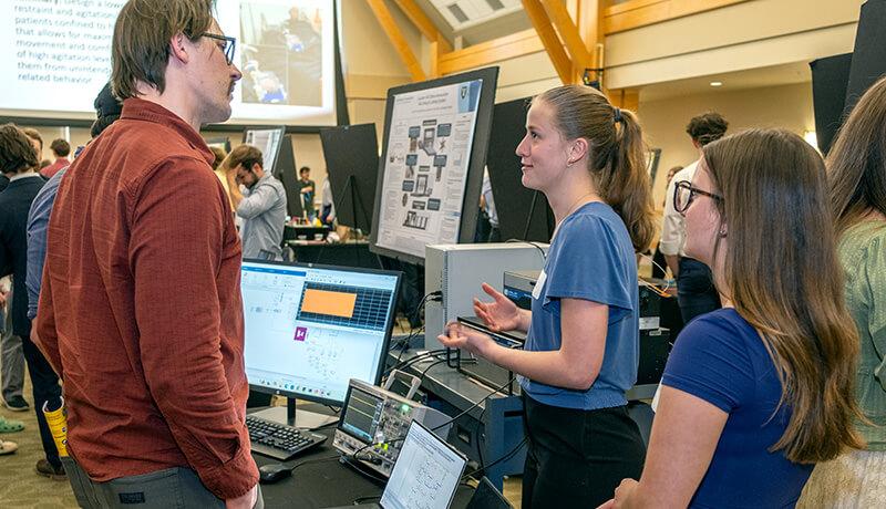 Team members Kendall Meienhofer and Janessa Green discuss the project they developed for VELCO, “Hardware in the Loop for Grid Resilience,” with Electrical Engineering senior lecturer Tony Barsic.