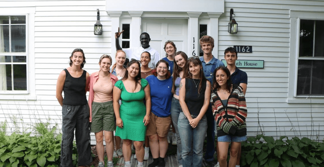 A group of students smiling in front of a white paneled house