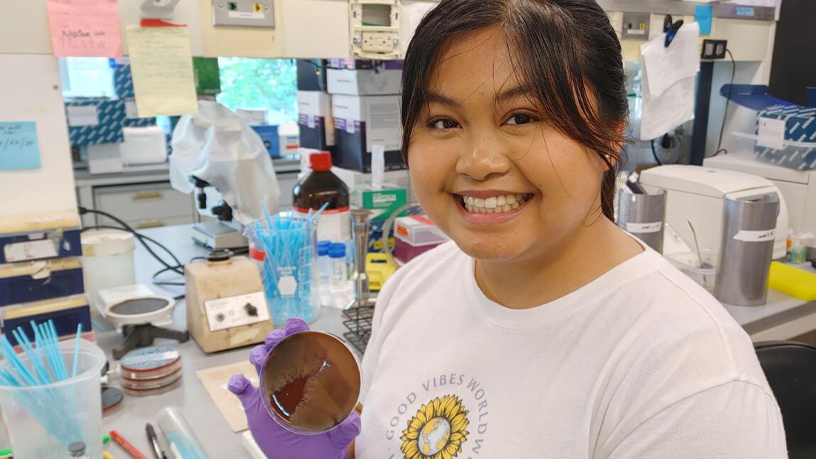 Graecia Pacheco in the Barlow Lab holding a plated bacteria specimen.