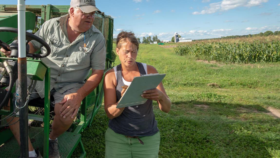 UVM Extension Professor and Agronomy Specialist Heather Darby talks to a man driving a tractor while working on a farm field.