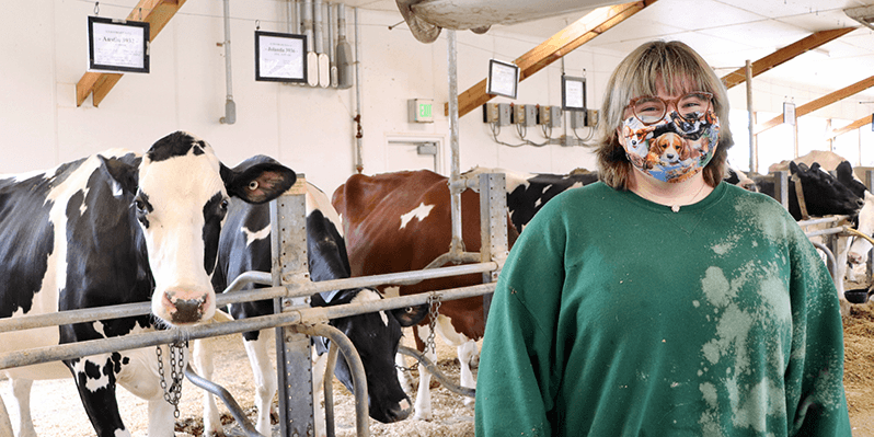 student standing in dairy barn with cows